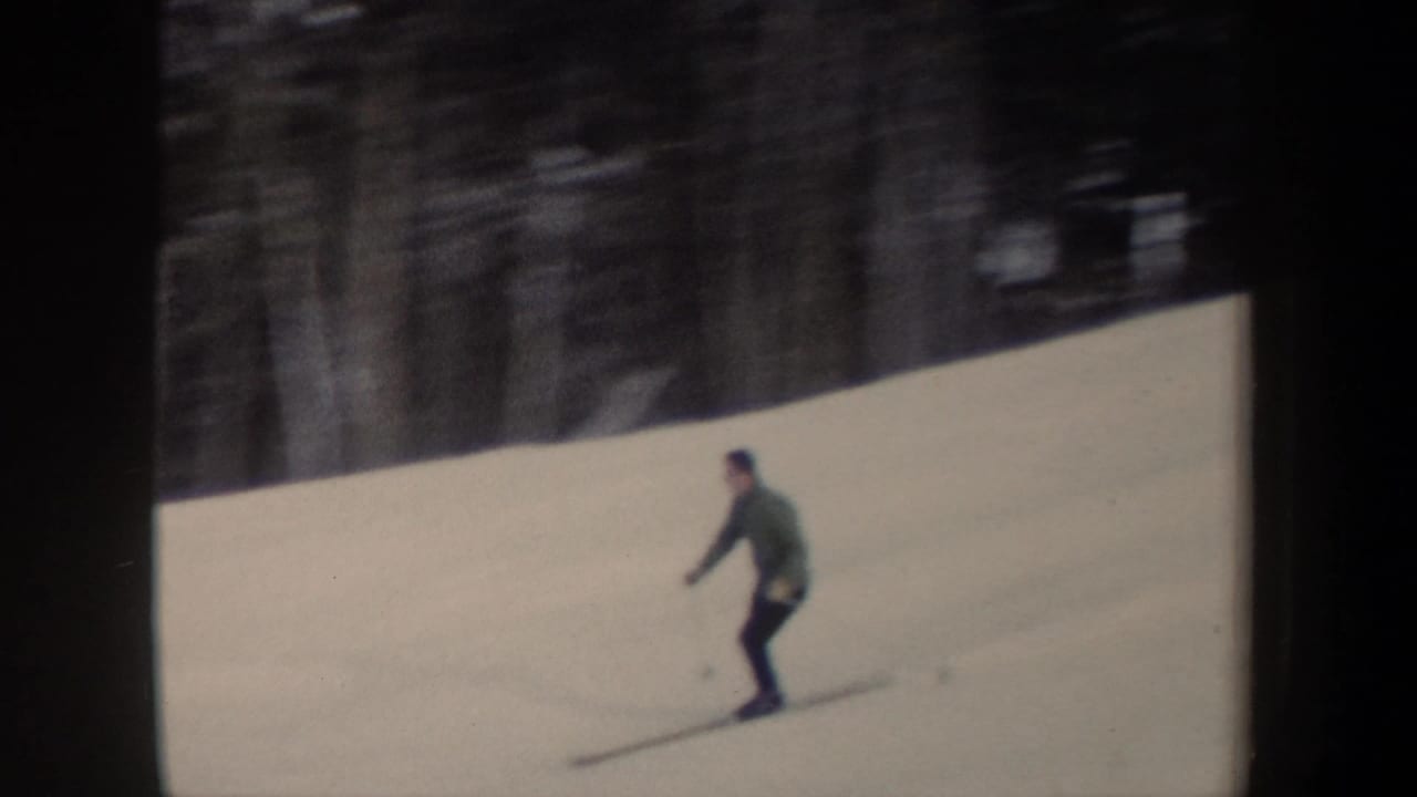 Skier in dark clothing gliding across a bright snowy hillside.