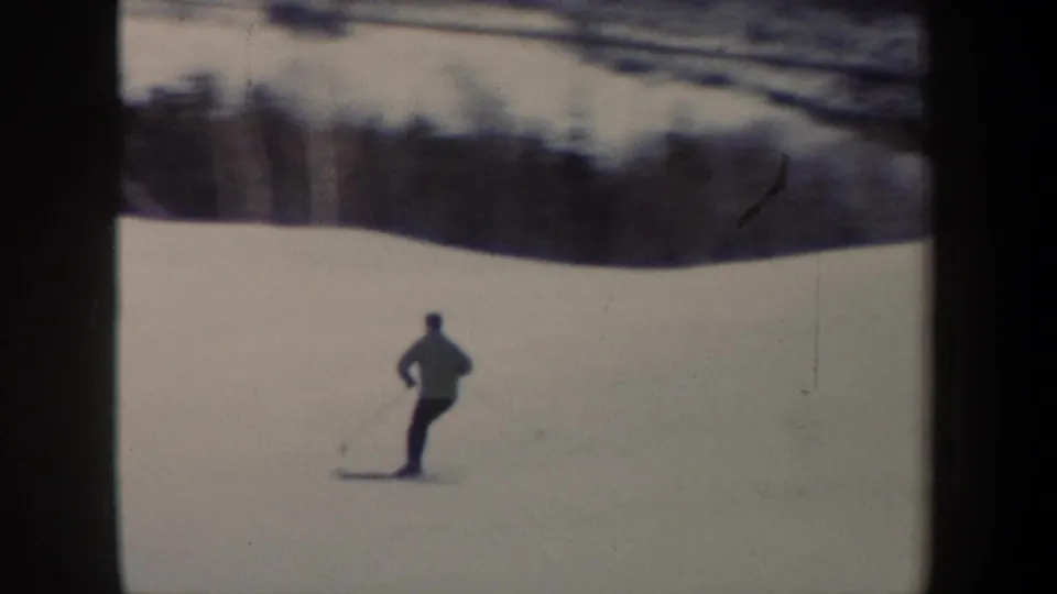 1962 New York 8mm frame showing the skier farther down the slope, filmed from behind with woods in the background.