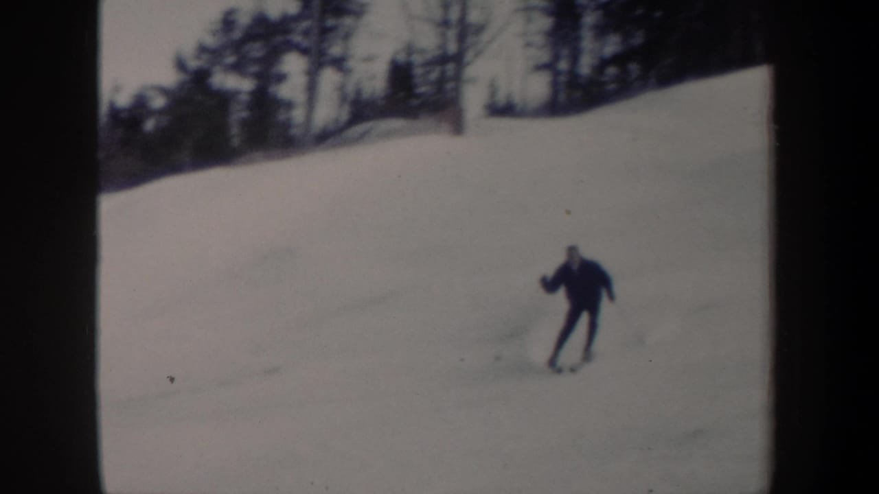 Skier in dark clothing turns across a snowy hillside.