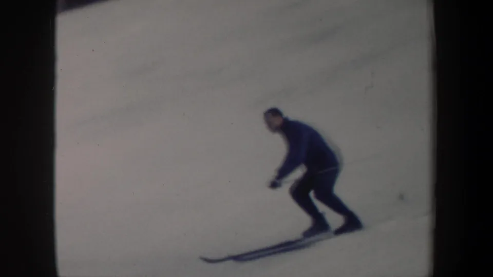 Closer 8mm frame of a skier crouching with poles while descending the snowy course in New York.