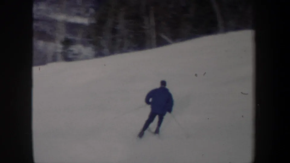 Rear view of the skier continuing downhill across an open snowy slope, with trees beyond the course.