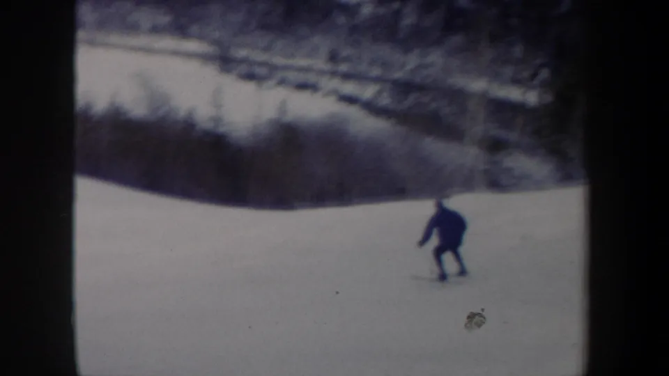 A distant skier in dark clothing moves downhill on a snowy New York slope in 1962 home-movie footage.