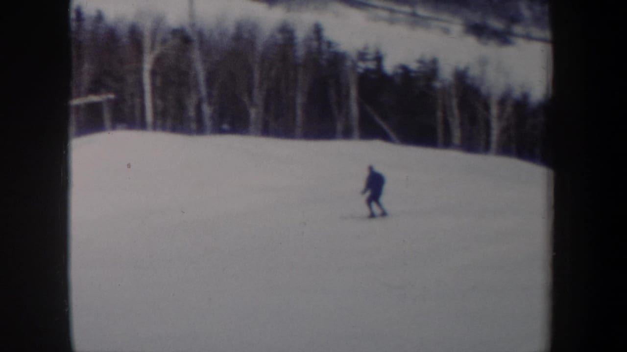 Skier crossing an open snowfield near a tree-lined slope.
