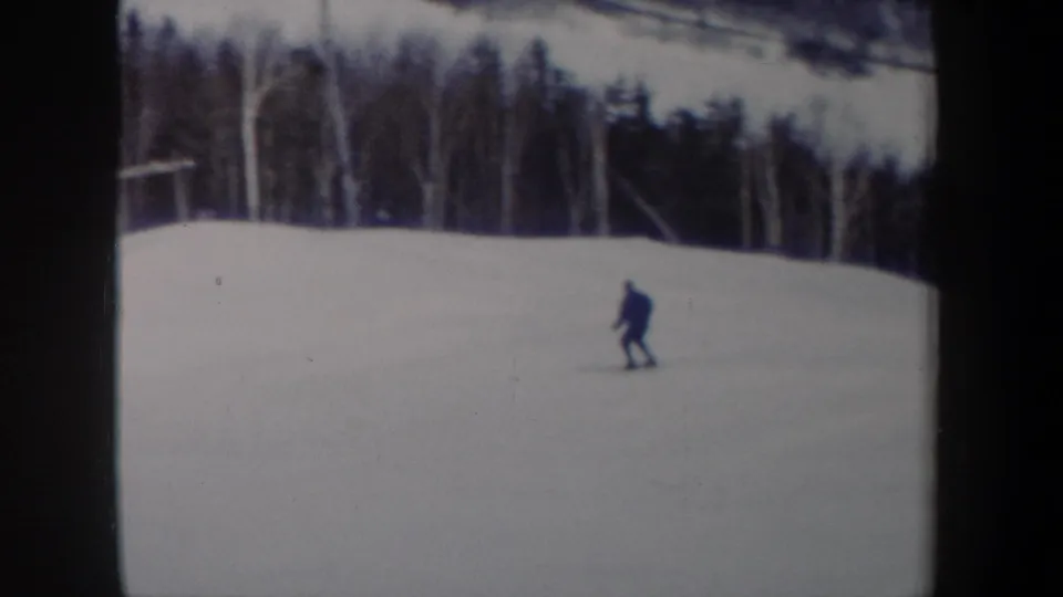 The skier appears small against an open snowy run, with a line of winter trees behind in 1962 New York footage.