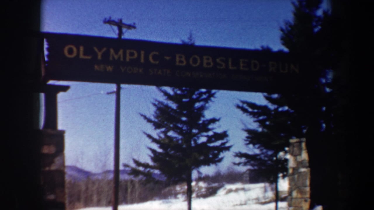 Entrance sign for Olympic Bobsled Run above snowy trees and stone gate posts.