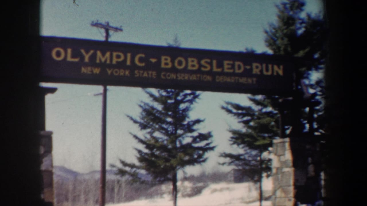 Olympic Bobsled Run sign framed by evergreens, snow, stonework, and a pale sky.