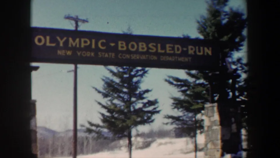 1962 New York 8mm frame with the Olympic Bobsled Run sign filling the upper view above evergreens, snow, and distant hills.