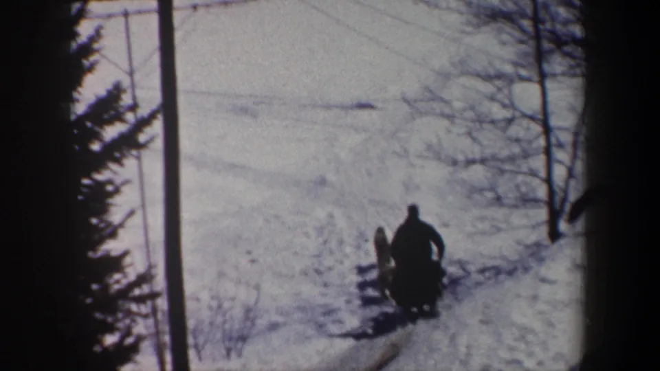 1962 New York 8mm frame showing a silhouetted sled rider and dog team moving away across a snow-covered route.