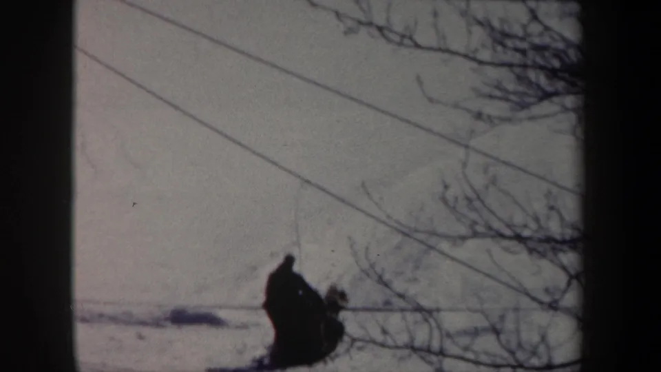 Final 1962 New York home-movie frame showing the musher and dogs receding across a snowy landscape beneath power lines.