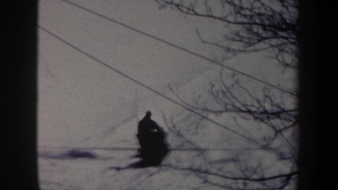 1962 New York 8mm frame showing a distant sled rider moving across a snowy field under bare branches and overhead lines.