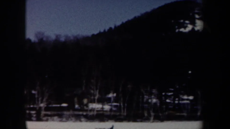 1962 New York 8mm frame looking toward a wooded snowy hillside with small houses and bare trees in the foreground.