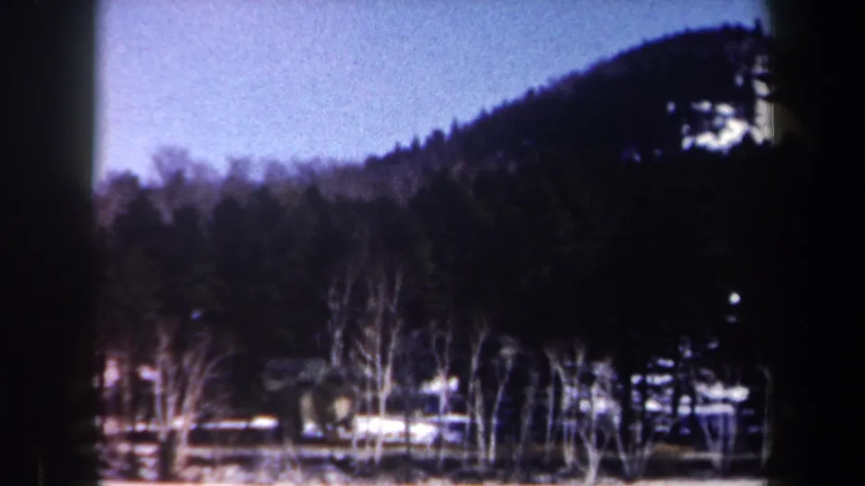 1962 New York home-movie frame showing a winter hillside, bare trees, fences, and scattered houses in soft focus.