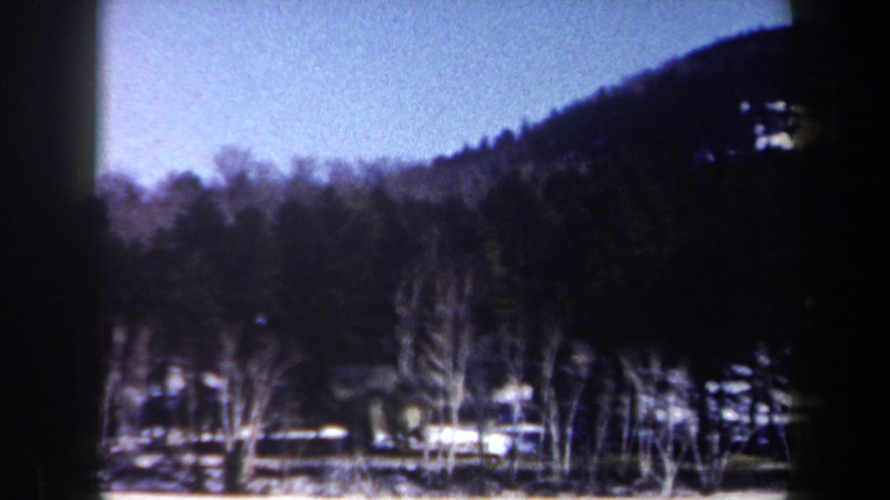 Dark forested hill and winter trees with snow along the lower edge of the frame.