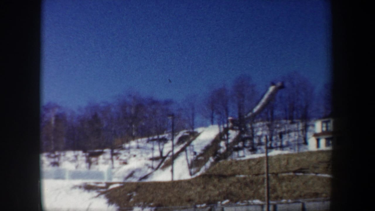 1962 New York 8mm frame showing a snow-covered hill and wooden ski jump structure beneath bare winter trees.