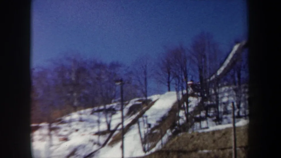 1962 New York 8mm frame showing the ski jump structure from a slightly closer spectator angle on a snowy hillside.