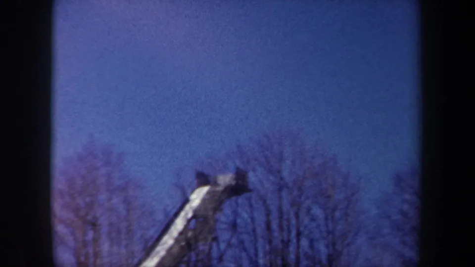 1962 New York 8mm view of a ski jump ramp partly obscured by winter trees under a blue sky.
