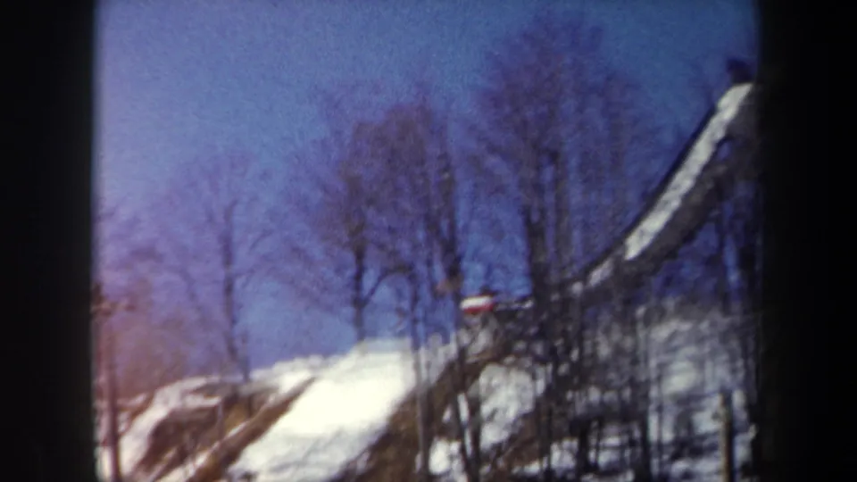 1962 New York frame showing the ski jump ramp beside a snowy slope, with a distant red figure or marker near the base.