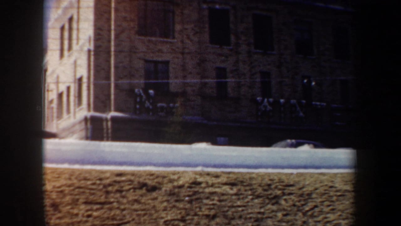 Snowy street in front of a brick building with large facade lettering and dark windows.