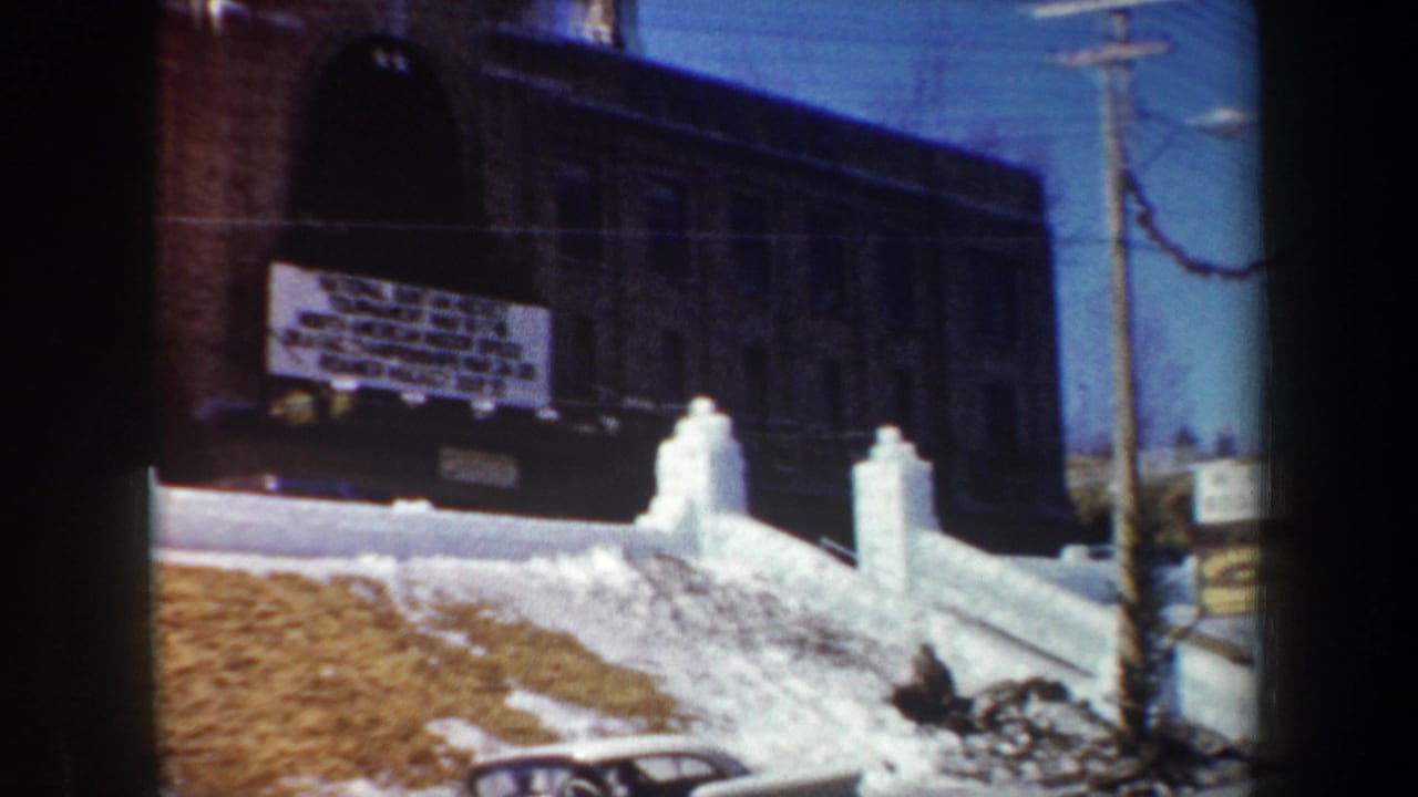 Brick school and white event sign seen behind snowbanks and a utility pole.