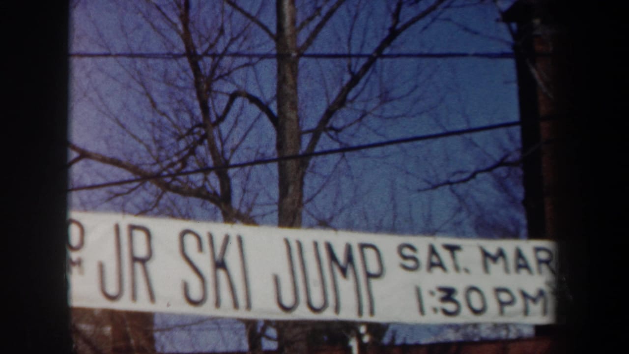 White banner reading JR SKI JUMP with bare trees and overhead wires behind it.