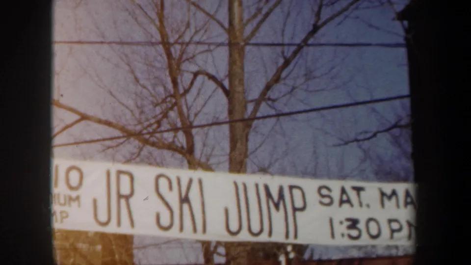 Final 8mm frame of the junior ski-jump banner in snowy New York, with Saturday date and 1:30 PM timing partly visible.