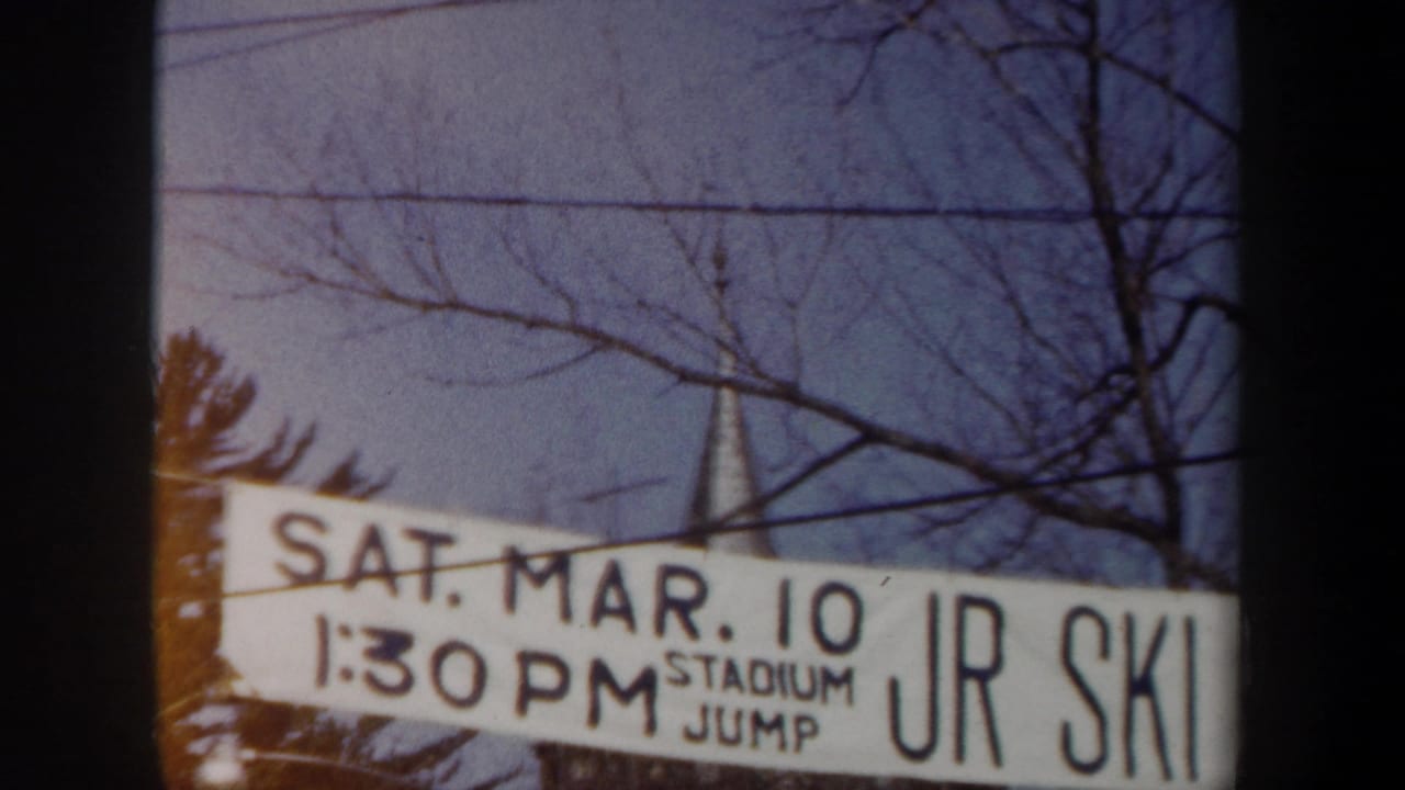 1962 New York home-movie frame with a white banner reading SAT. MAR. 10 and STADIUM JUMP JR SKI near winter trees.