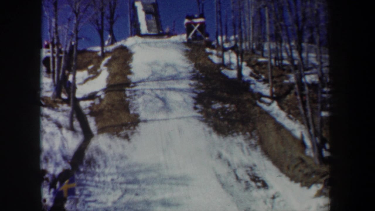 1962 New York 8mm frame showing a snow-covered ski-jump slope, bare trees, wooden jump structure, and small Swedish flag.