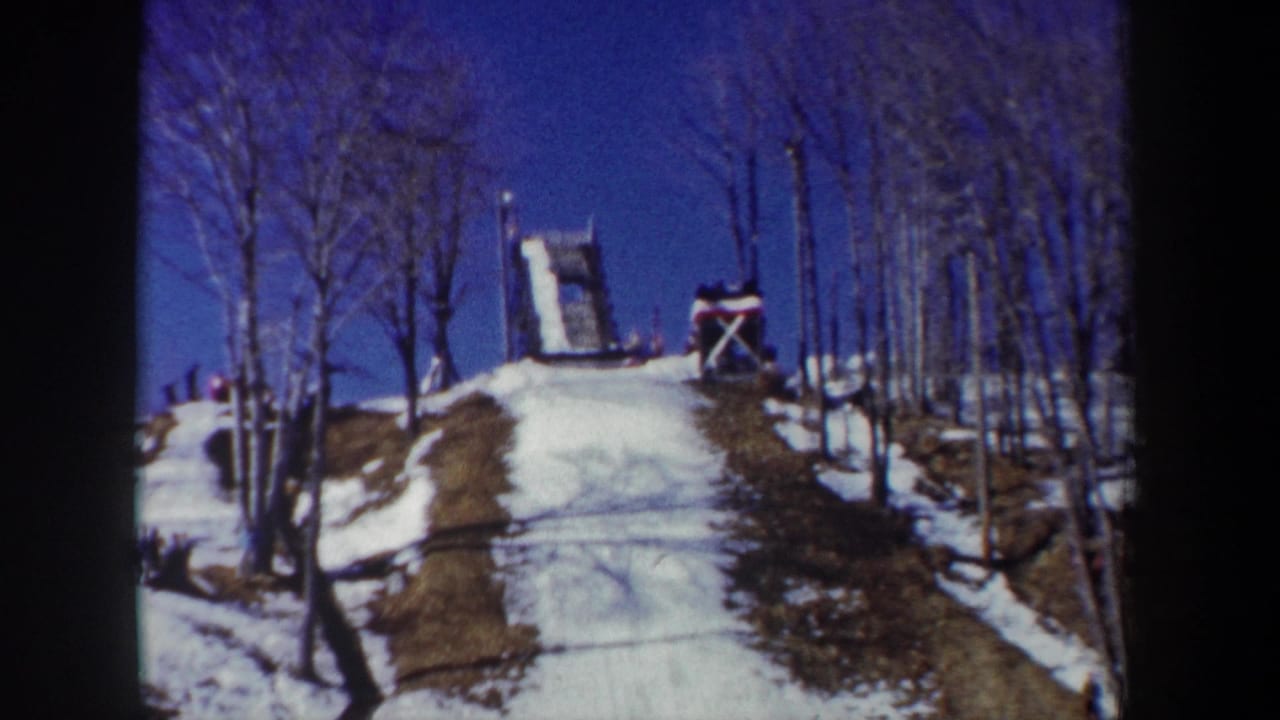 1962 New York 8mm frame of a snowy ski-jump hill with leafless trees and the wooden ramp structure near the crest.