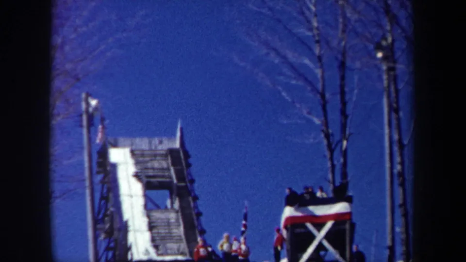 1962 New York 8mm frame showing the ski-jump tower and distant people gathered near a flag at the top area.