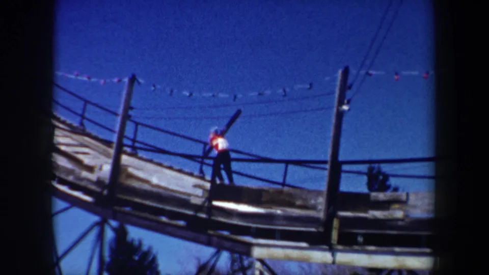 1962 New York 8mm frame showing a skier with skis on a wooden ski-jump platform, with posts and lines visible overhead.