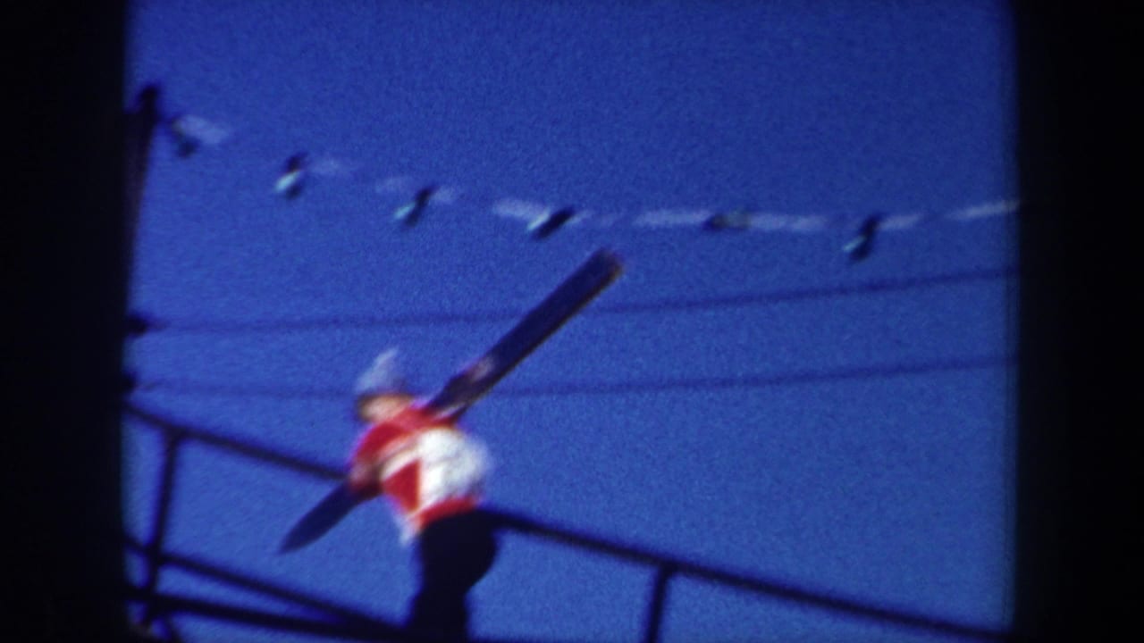 1962 New York home-movie frame showing a man in a red and white jacket carrying skis on a metal stairway below utility lines.