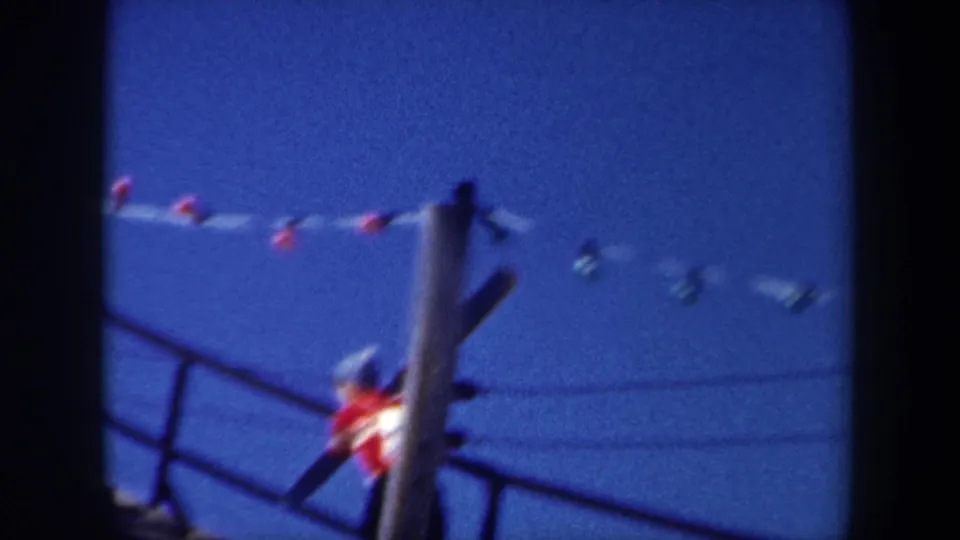 Home-movie frame from the 1962 New York clip showing a skier partly obscured by a pole while climbing with skis.