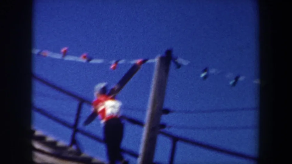 Final 1962 New York frame showing the skier on metal steps, skis over the shoulder, with poles and wires above.