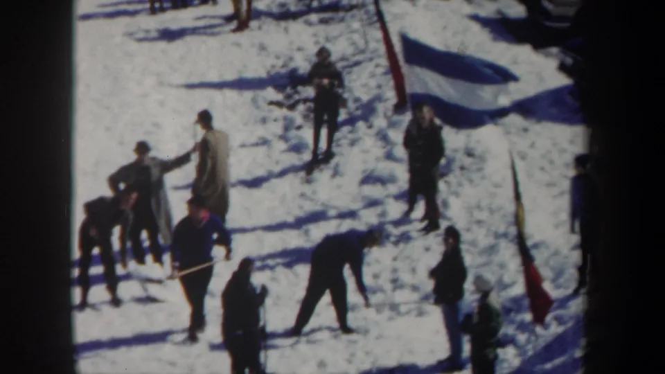 1962 New York home-movie frame of people in coats and hats working or standing on snow near planted marker flags.