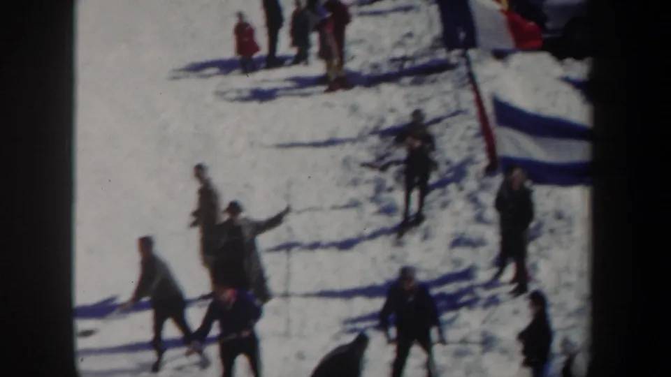 1962 New York 8mm frame showing people moving across snow near a red pole and blue-and-white flag marker.