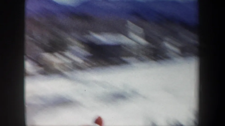 Soft, motion-blurred 1962 New York ski-jump frame with a moving skier or figure crossing the snowy foreground.