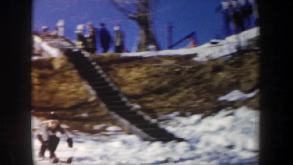 1962 New York 8mm frame with a skier near the bottom of a snowy ski-jump hill and spectators above.