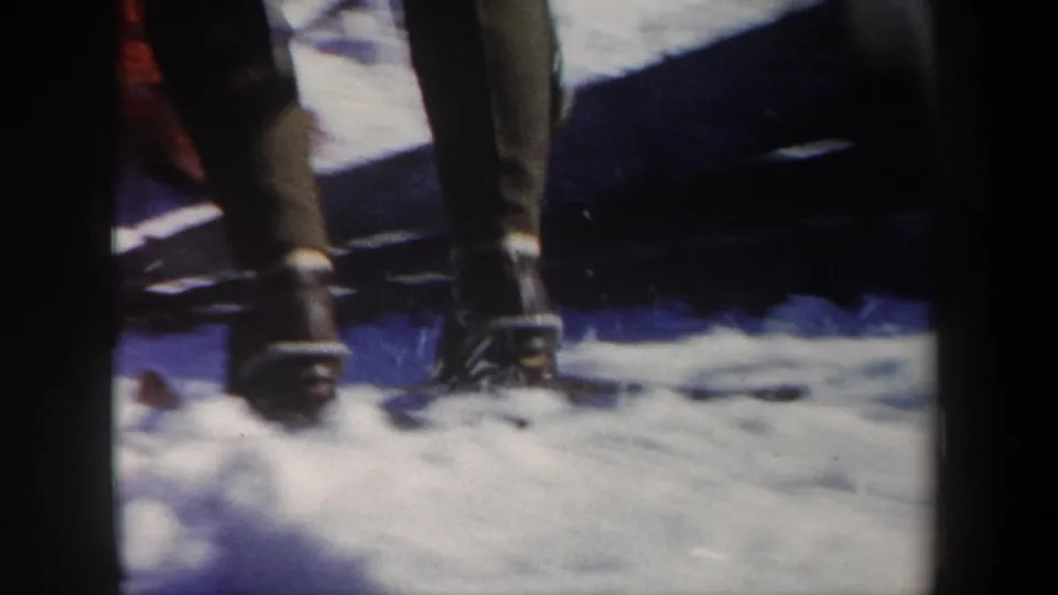 Close home-movie view of winter boots and trouser legs moving through deep snow at the New York ski-resort setting.