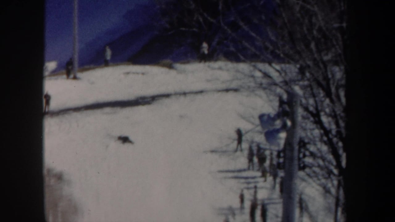 Distant snowy slope with spectators, bare trees and dark film-frame borders.