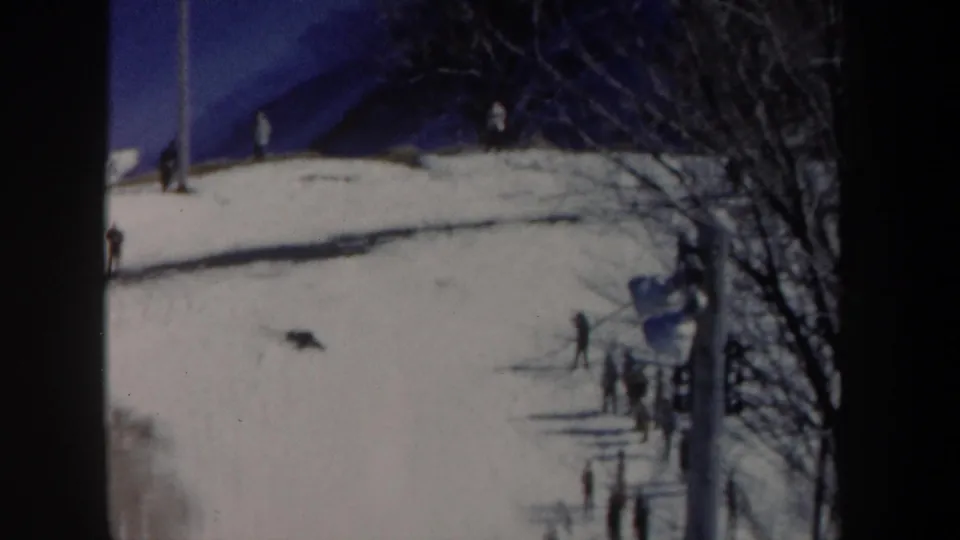 1962 New York home-movie view of a snowy ski area with distant spectators, bare trees and heavy 8mm frame borders.