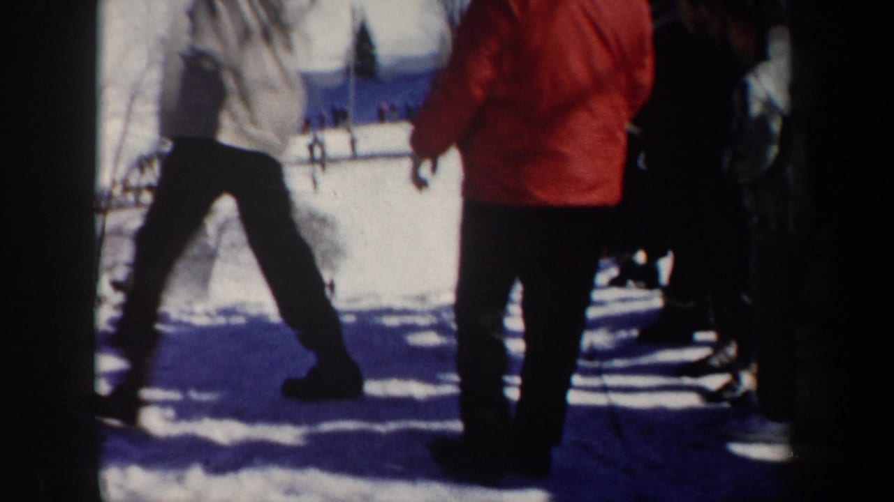 Spectators stand beside a snowy ski slope as a person in red winter clothing faces the course.