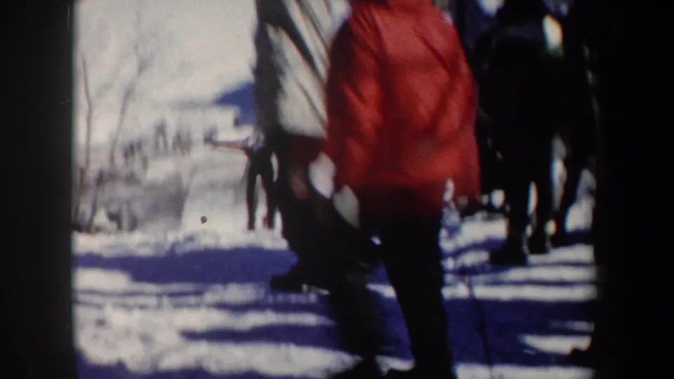 Bibbed skier on a snowy New York slope in 1962, filmed from a spectator area with winter-clothed people nearby.