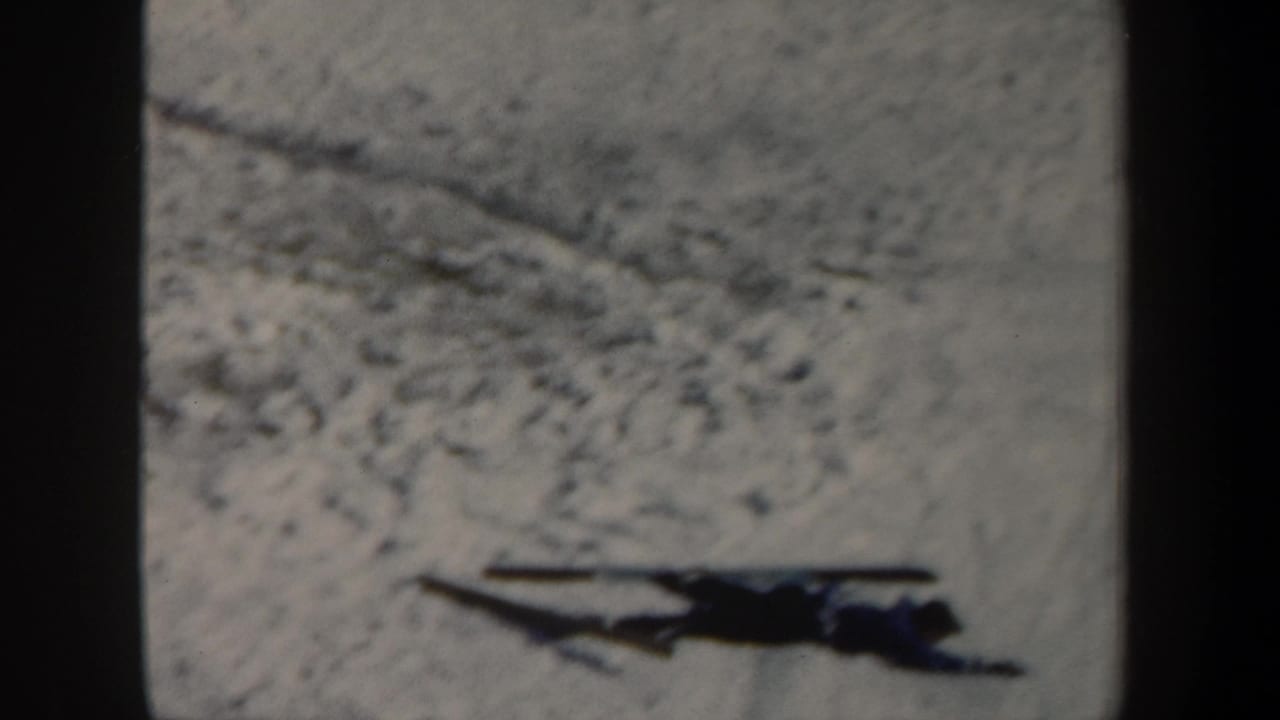 Skier remains stretched out on the snow near a small jump landing area.