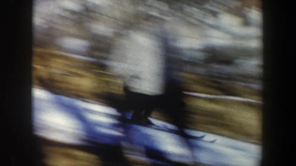 Blurred 1962 New York ski action shows a skier moving quickly across snow, with hillside colors and winter trees behind.