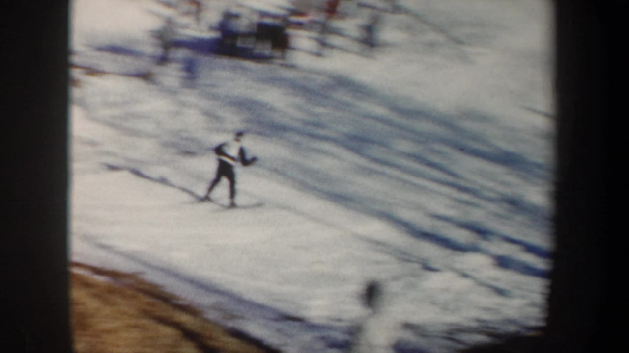1962 New York 8mm frame showing a skier on a snowy slope, with spectators faintly visible near the top of the hill.