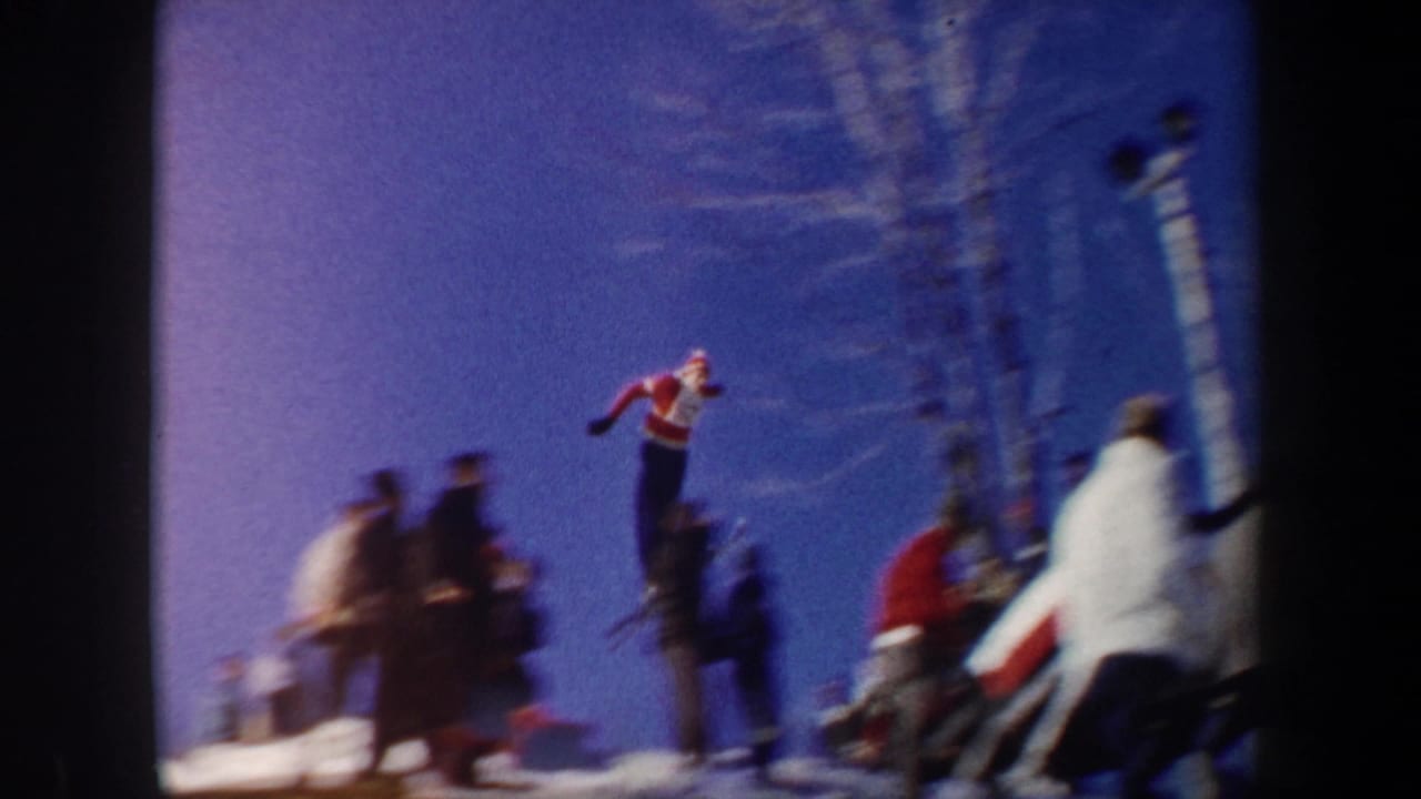 Ski jumper airborne above spectators against a bright blue sky.