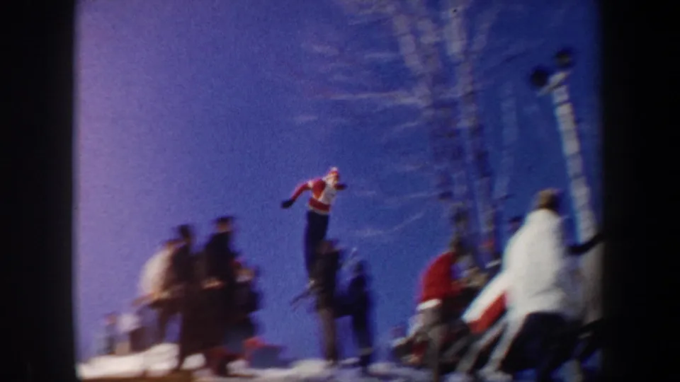 1962 New York 8mm frame with a red-and-white dressed ski jumper in the air above a snowy spectator area.
