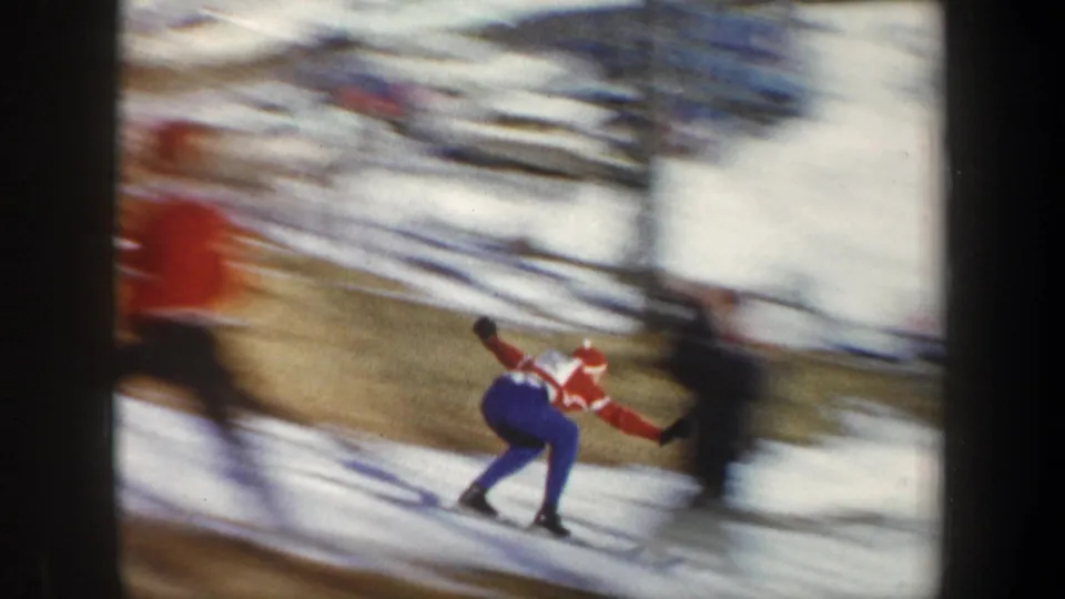 1962 New York 8mm frame showing the ski jumper landing or sliding downhill as spectators blur at the edge of the slope.