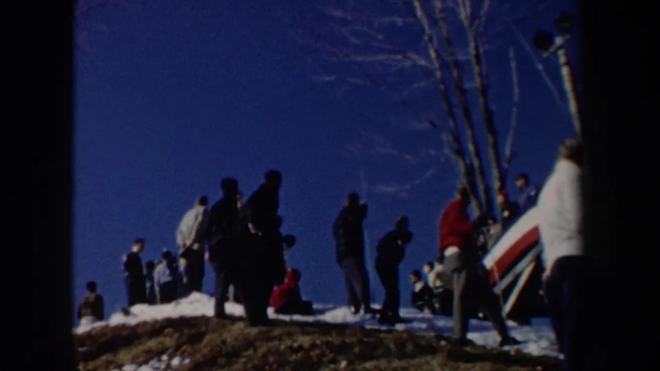 1962 New York 8mm frame showing spectators gathered along a snowy hillside after the ski-jump action.