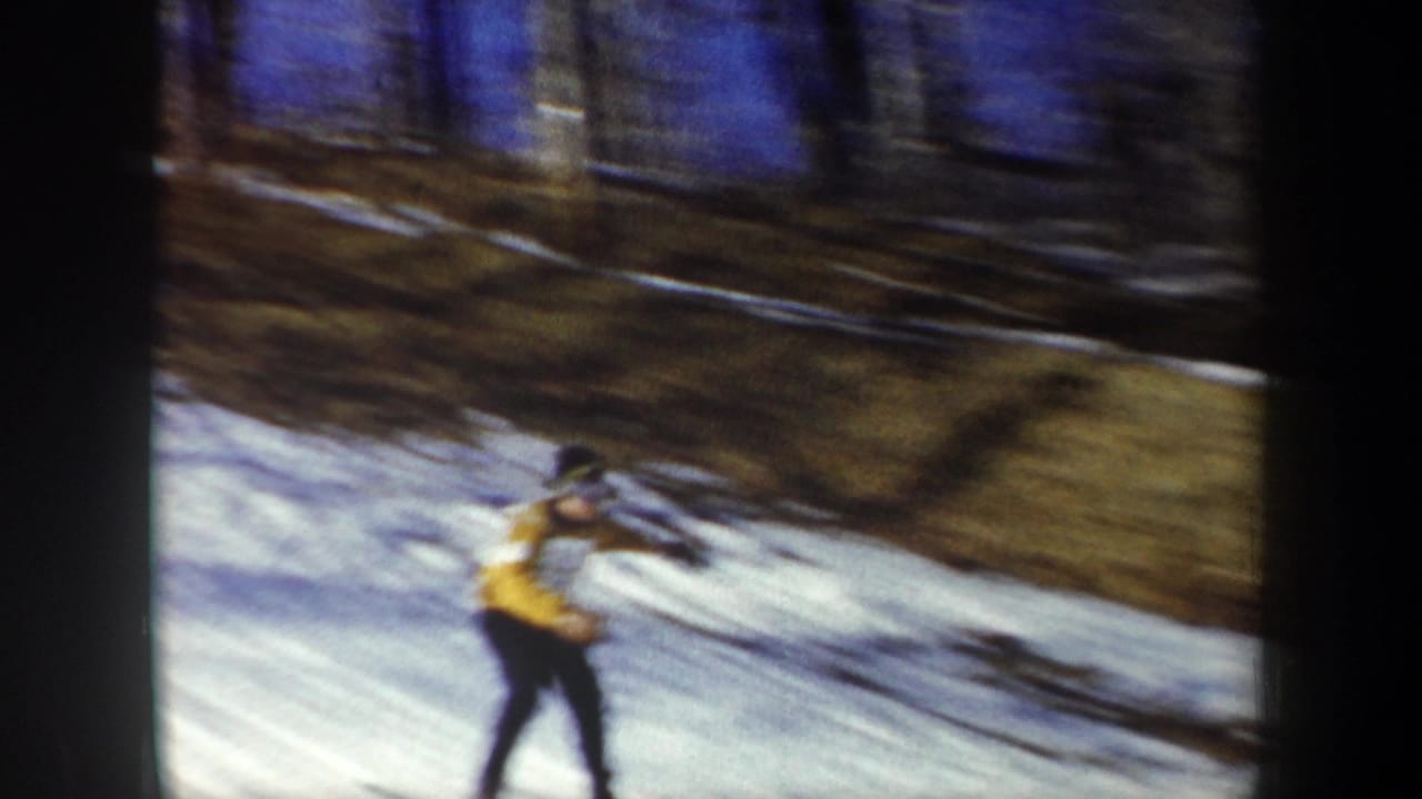 1962 New York 8mm frame showing a skier in yellow and dark clothing moving downhill on snow, blurred by motion.